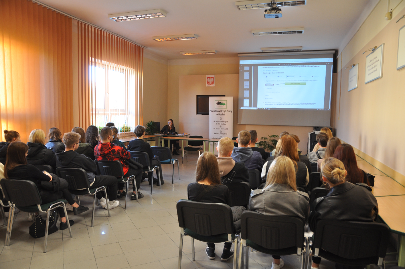 Sala konferencyjna, uczestnicy spotkania informacyjnego, na dalszym planie prowadząca spotkanie.