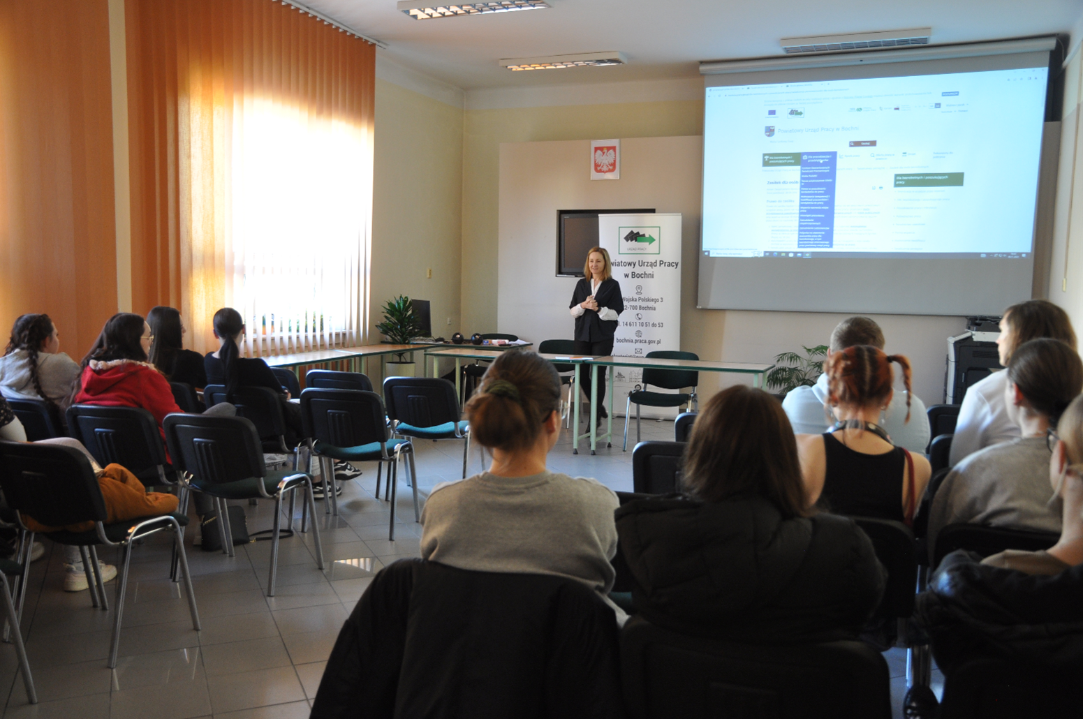 Sala konferencyjna Powiatowego Urzędu Pracy w Bochni, uczestnicy spotkania informacyjnego, na dalszym planie prowadząca spotkanie.